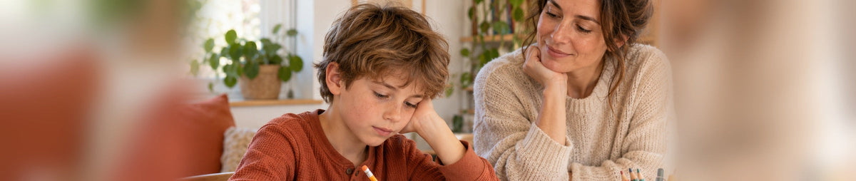 Enfant accompagné par un parent pendant les devoirs avec casque anti-bruit, fidget et timer visuel sur la table