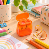 Taille-crayon ergonomique orange à deux trous ouvert sur un bureau avec crayons et copeaux.