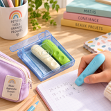 Gommes ergonomiques à encoches bleu, beige et vert dans leur boîte, avec une gomme bleue utilisée sur un cahier.